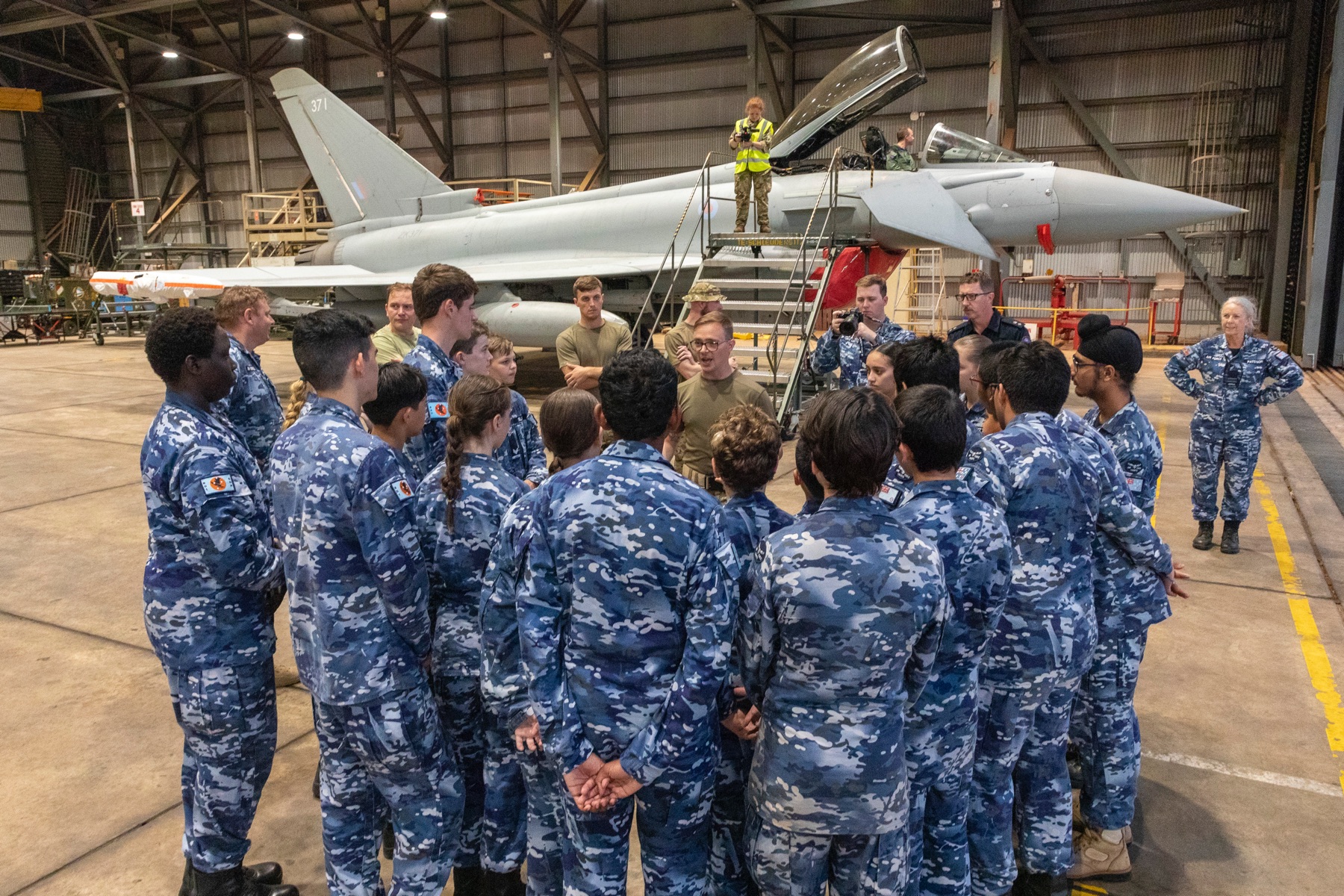 Image shows group of Royal Australian Air Force personnel in hangar with RAF Typhoon in background.